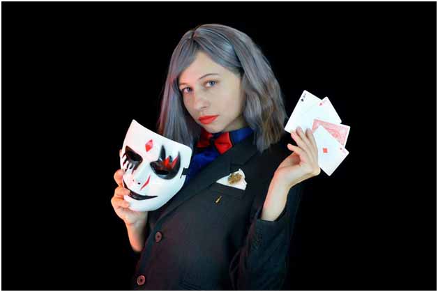 A woman with grey hair in a suit holding a mask and cards
